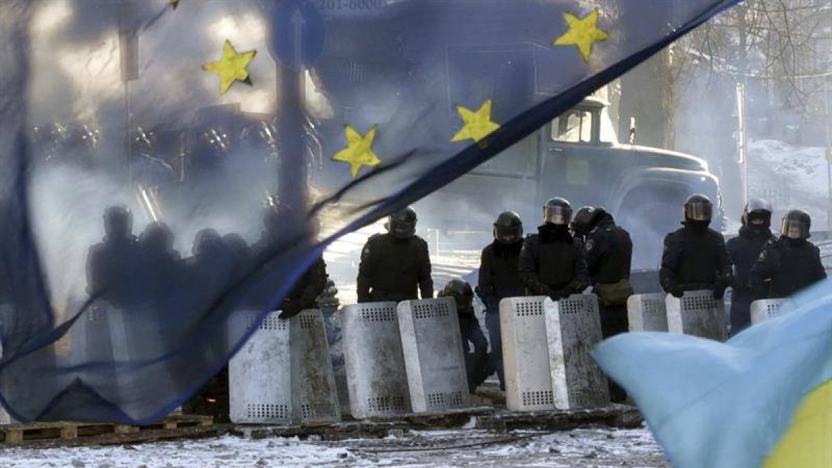 Varios policías antidisturbios montan un cordon policial tras una bandera de la Unión Europea cerca de una de las barricada un nuevo día de protestas contra el gobierno en el centro de Kiev