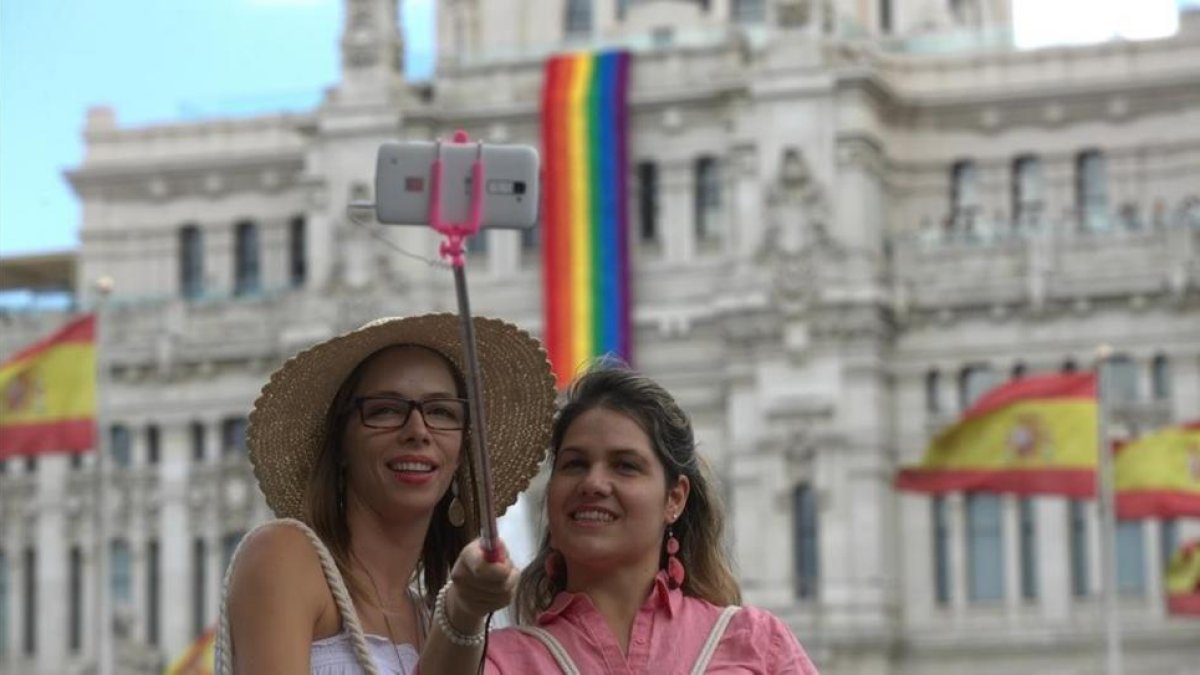 Dos turistas se hacen un 'selfie' frente al Ayuntamiento de Madrid, que luce la bandera del arcoiris en homenaje al World Pride 2017.