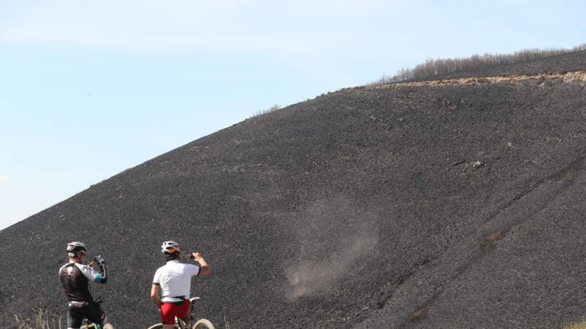 Dos ciclistas observan la montaña quemada por el fuego, el 21 de abril de 2017. ANA F. BARREDO