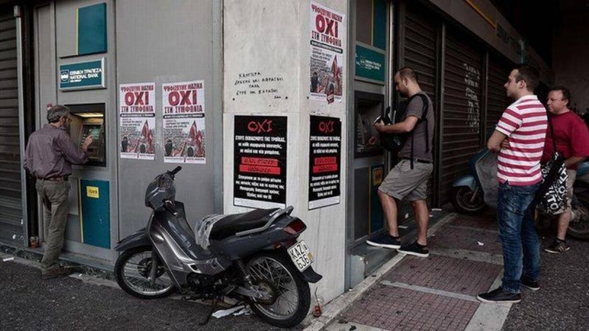 Colas ante cajeros en Atenas, con carteles a favor del 'no' en el referendum.