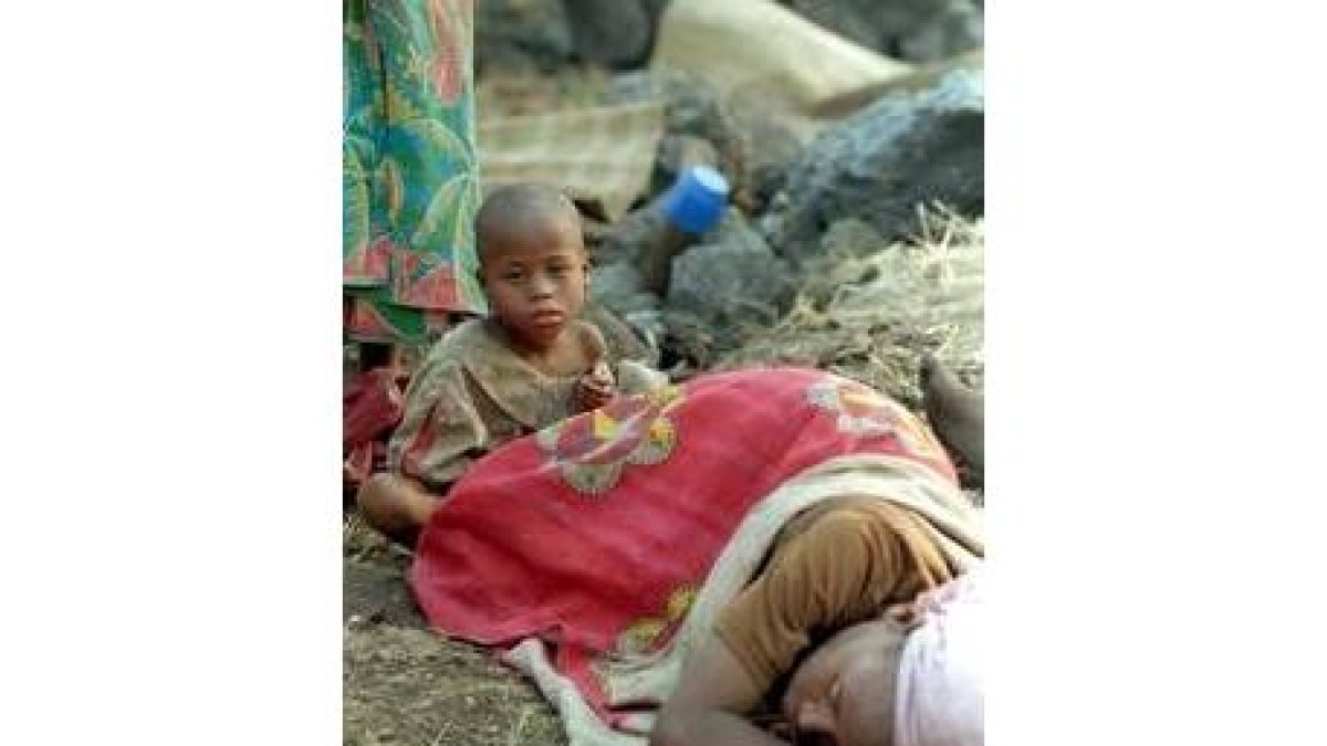 Un niño, sentado junto a su madre, mientras ésta descansa en el suelo, en un campo de refugiados