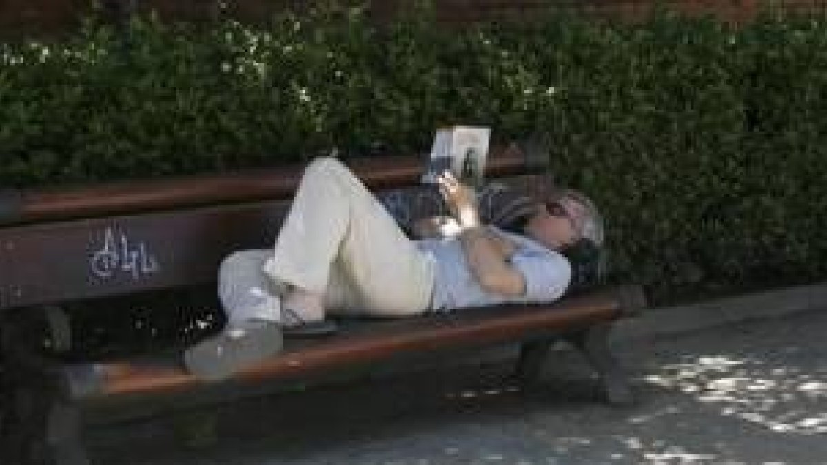 Un hombre descansa en un banco mientras lee un libro