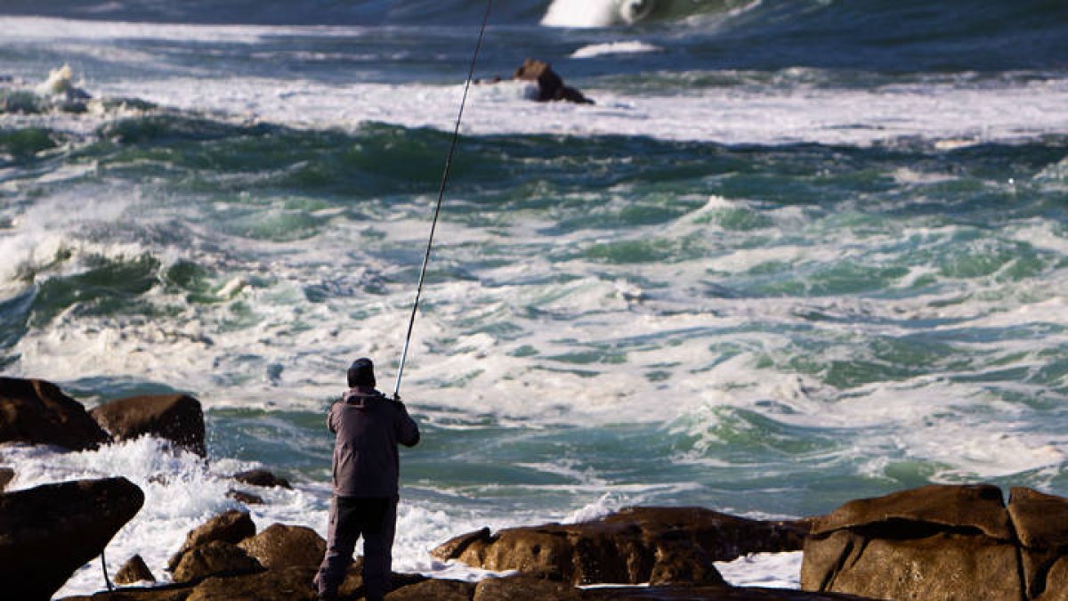 Un pescador lanza su caña sobre el mar picado en la playa de Santa María de Oia (Pontevedra). SALVADOR SAS