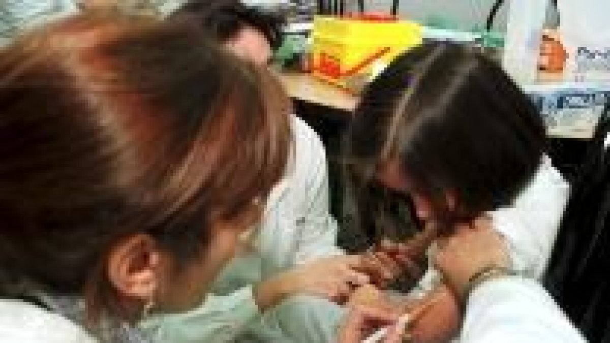 Dos sanitarias vacunan a un niño en un centro escolar