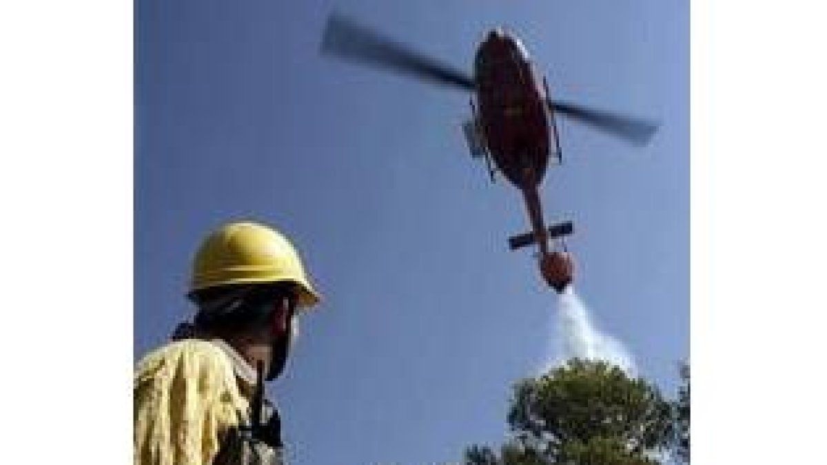 Un helicóptero descarga agua ante la mirada de un brigada forestal