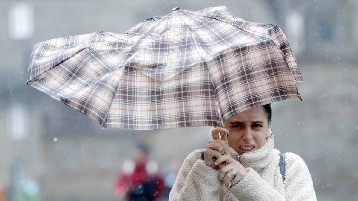 Una mujer se protege de la lluvia y el viento con un paraguas. LAVANDEIRA JR