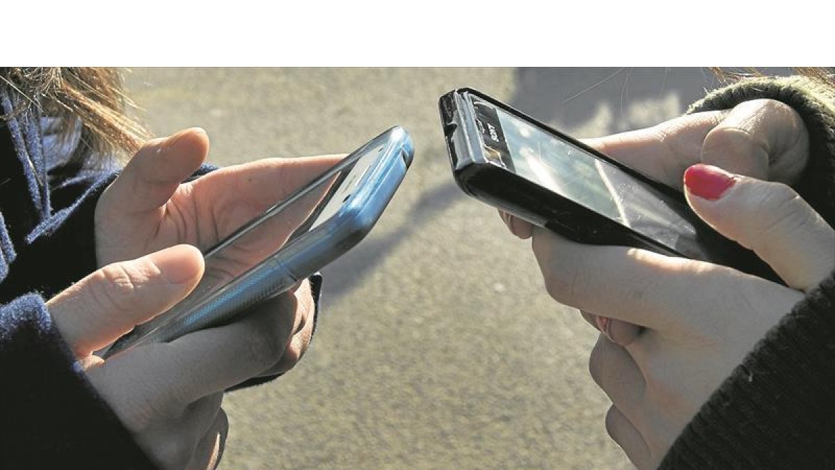 Dos jóvenes hacen uso de su teléfono móvil.