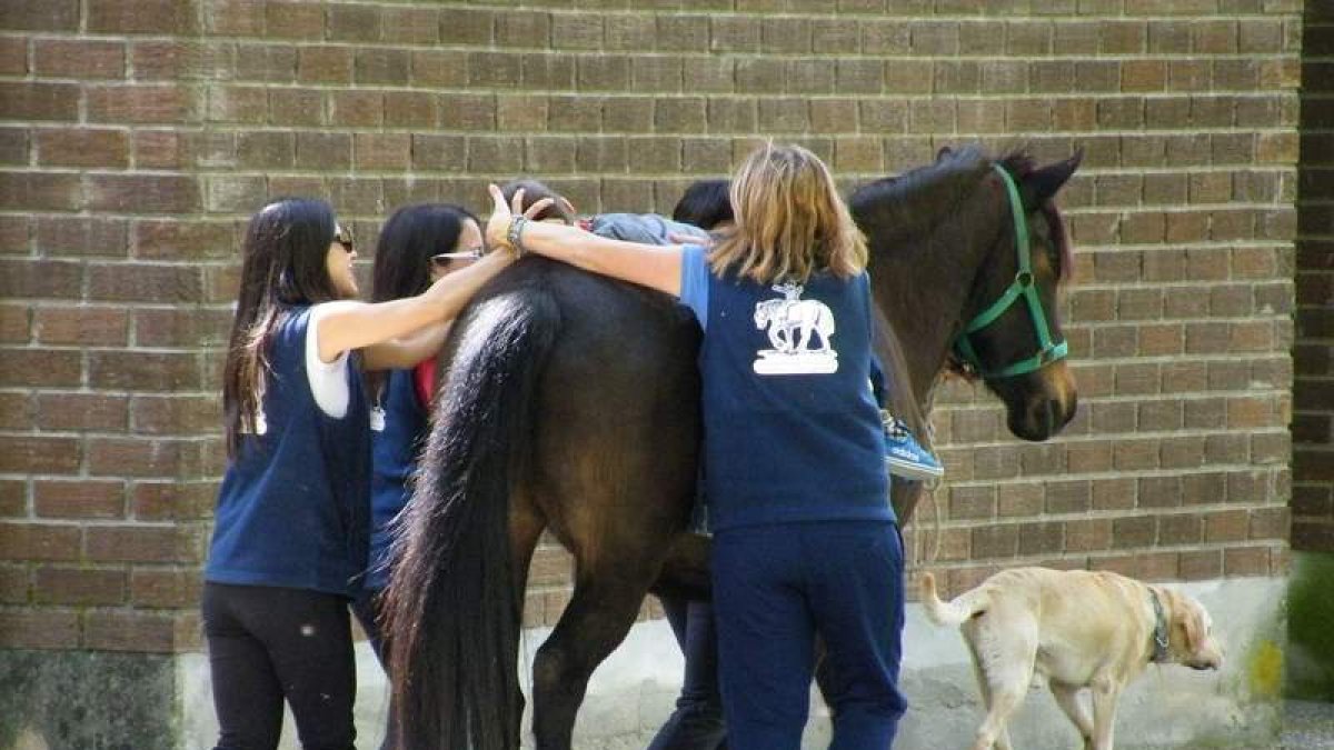 El caballo Cartucho lleva a uno de los niños, ayudado por monitoras de la asociación. DL