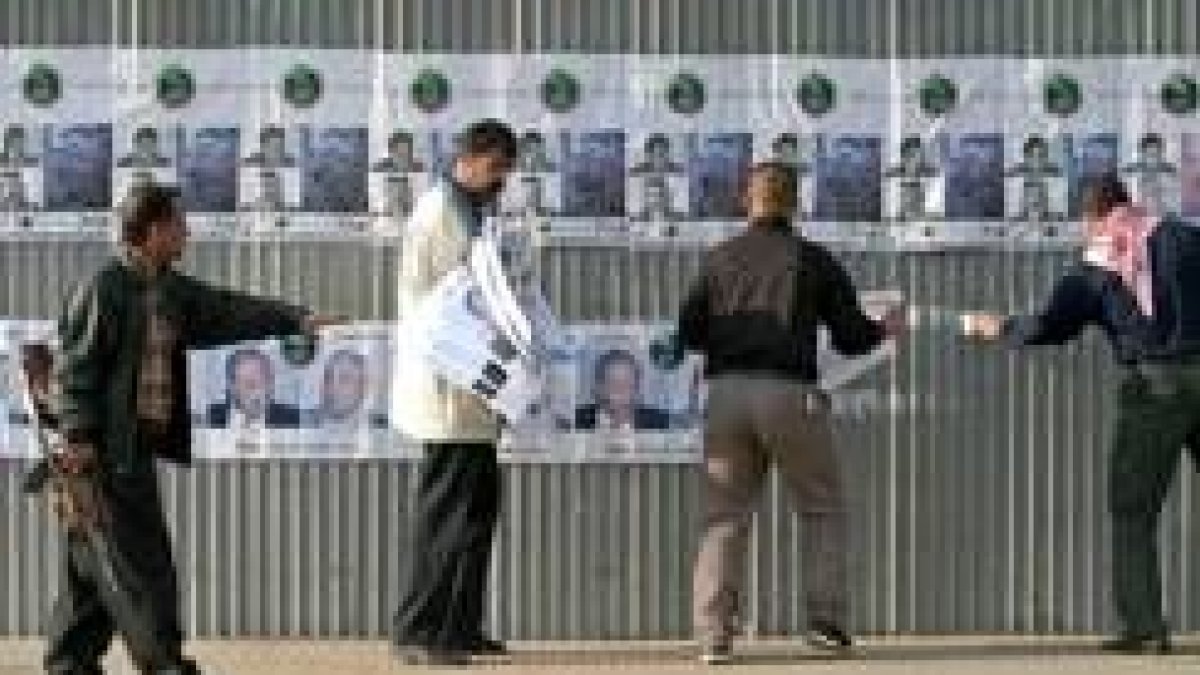 Un policía iraquí vigila a tres ciudadanos que colocan propaganda electoral en una calle de Bagdad
