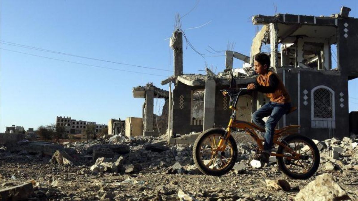 Un niño yemení pasea con su bicicleta junto a los escombros de una vivenda en Saná destrozada por los bombardeos aéreos.