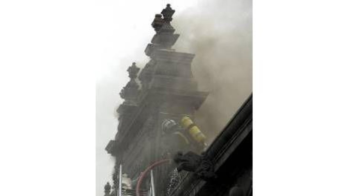 Un bombero intenta apagar las llamas subido en la fachada principal