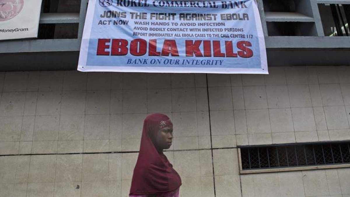 Una mujer pasa bajo un anuncio de alerta sobre el virus del Ébola en Freetown (Sierra Leona).