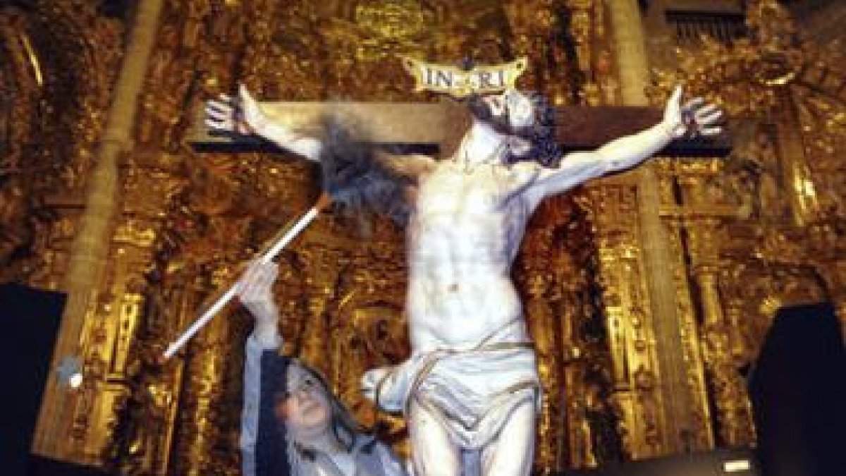 Una operaria limpia el polvo a un Cristo que se expone en la iglesia de Santiago de los Caballeros.