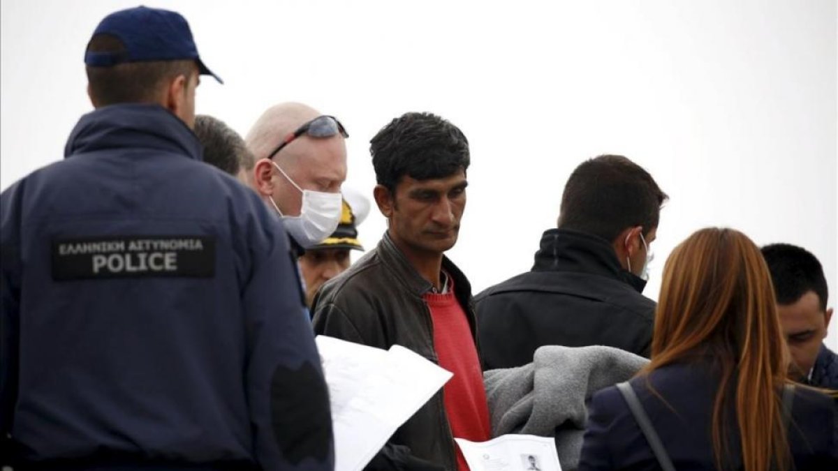 Un funcionario de la UE sostiene la documentación de un migrante (centro) en un barco que les traslada de regreso a Turquía desde Lesbos, este viernes.