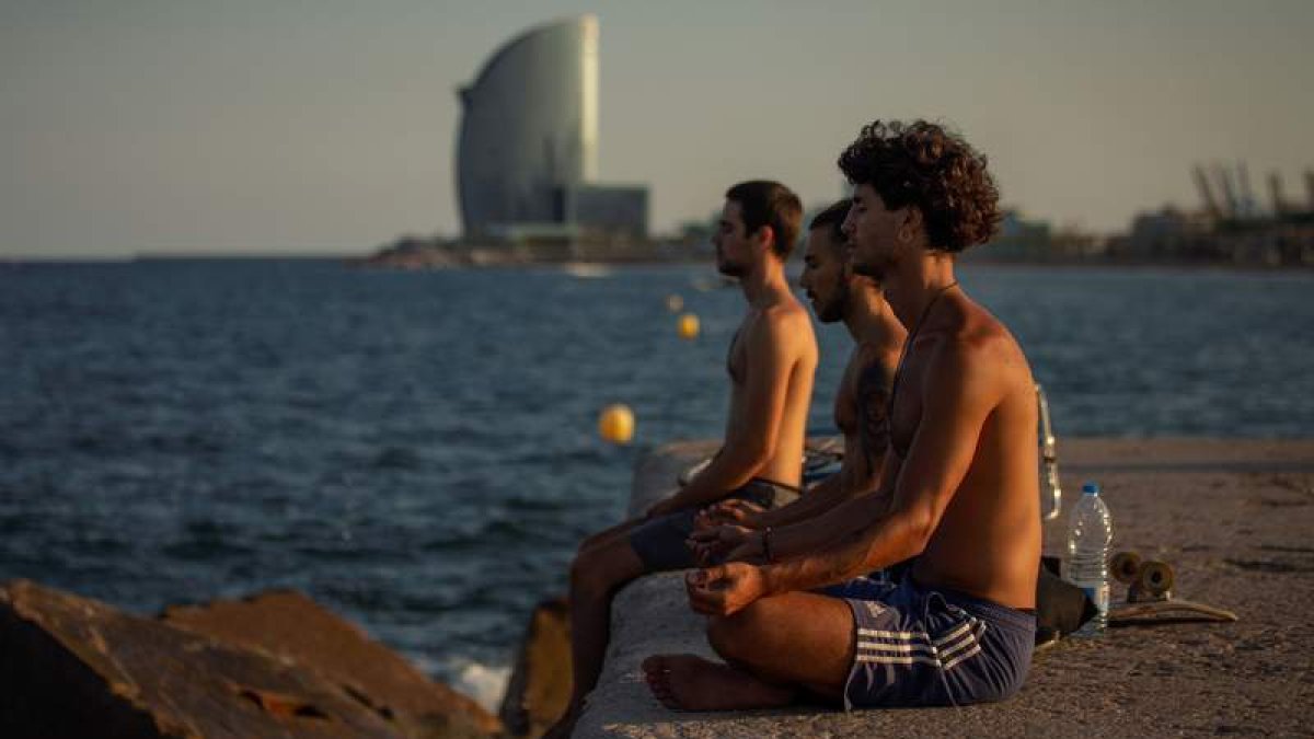 Tres jóvenes practican yoga al atardecer y frente al mar en el popular espigón del Gas de Barcelona. ENRIC FONTCUBERTA