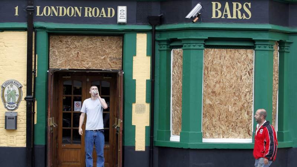 Un cliente bebe a las puertas de un bar con las ventanas protegidas en el barrio londinense de Croydon.