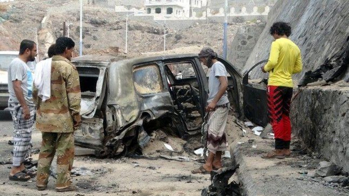 Varias personas contemplan los efectos del atentado con coche bomba en el que ha muerto el gobernador de Aden.