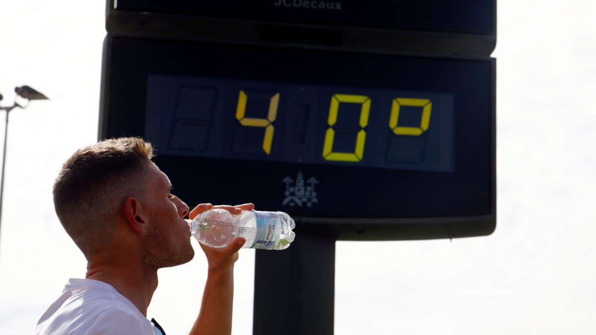 Un joven bebe agua junto a un termómetro de calle que marca 40 grados. EFE/SALAS
