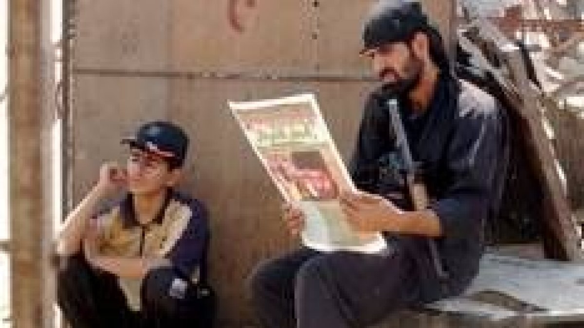 Dos hombres armados leen la prensa iraquí en el día de oración en Ciudad de Al Sáder