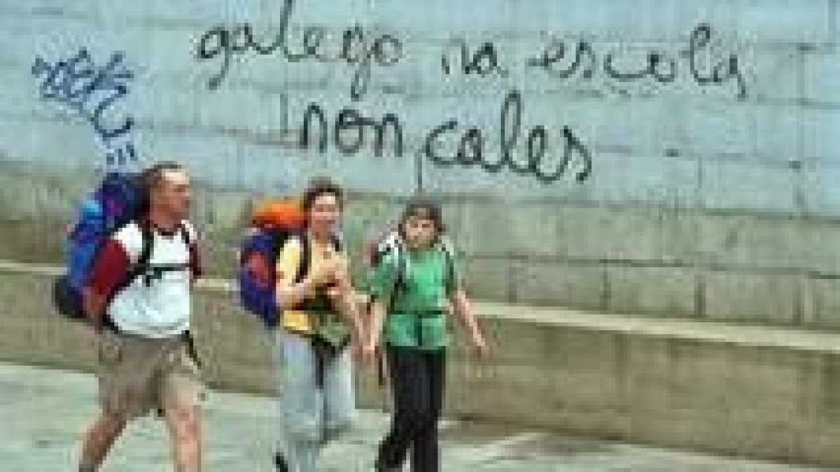 Tres peregrinos pasan delante de una pintada a favor de la enseñanza del gallego en las escuelas