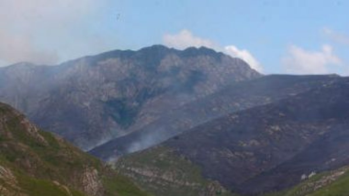 Un helicóptero sobrevuela la zona arrasada por el fuego, colindante con otra parte de la montaña.
