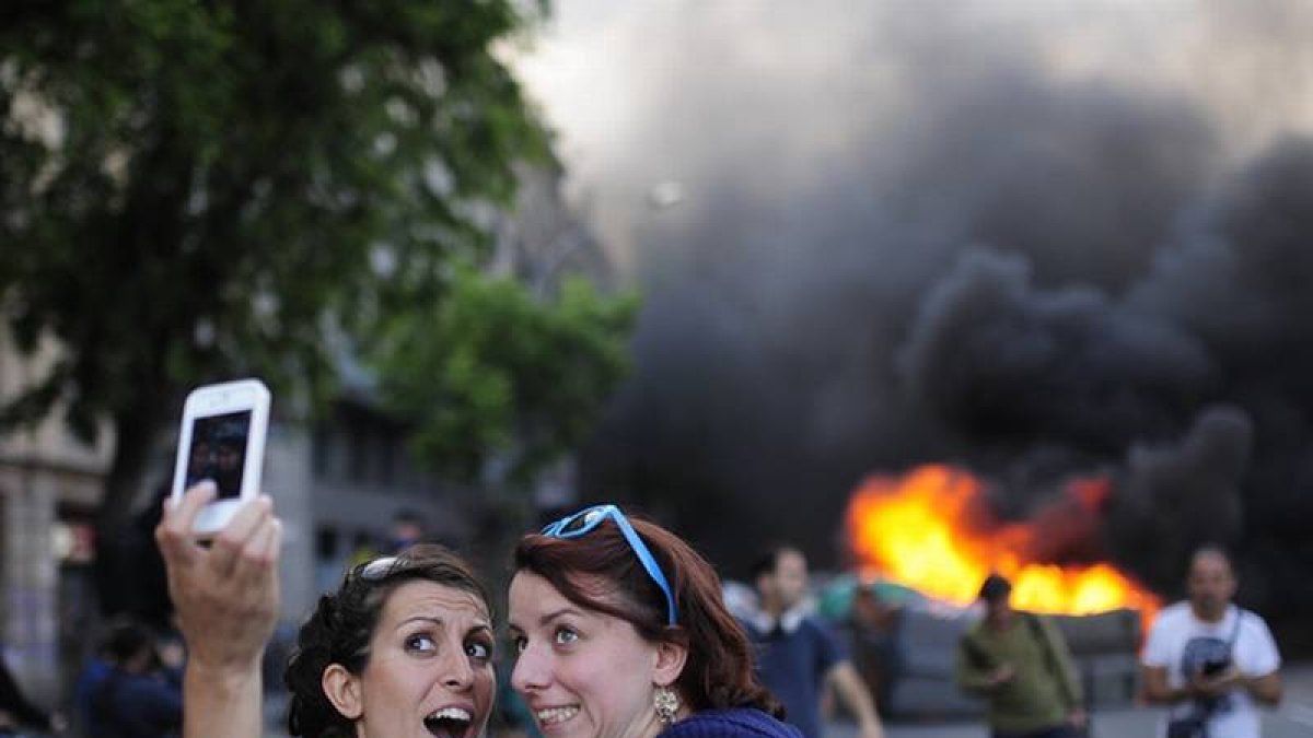 Unas turistas se hacen un 'selfie' con unos contenedores ardiendo de fondo este jueves, en Barcelona.