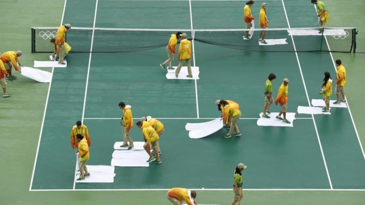 Voluntarios secan con toallas la pista central, en Río de Janeiro.