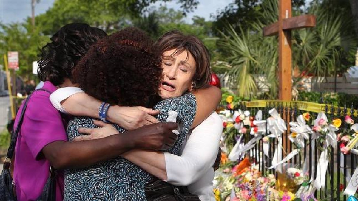 Tres mujeres se abrazan junto a la ofrenda floral frente a la iglesia metodista, en Charleston, este sábado.