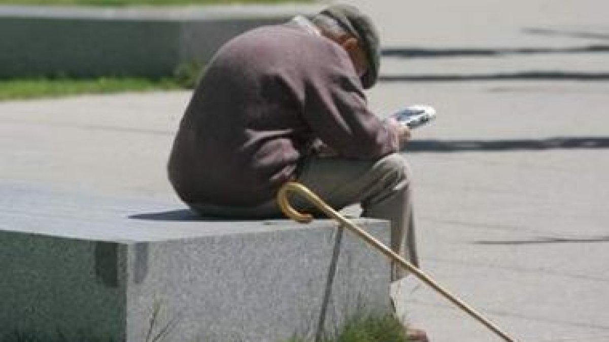 Un anciano lee el periódico sentado en uno de los parques de León.