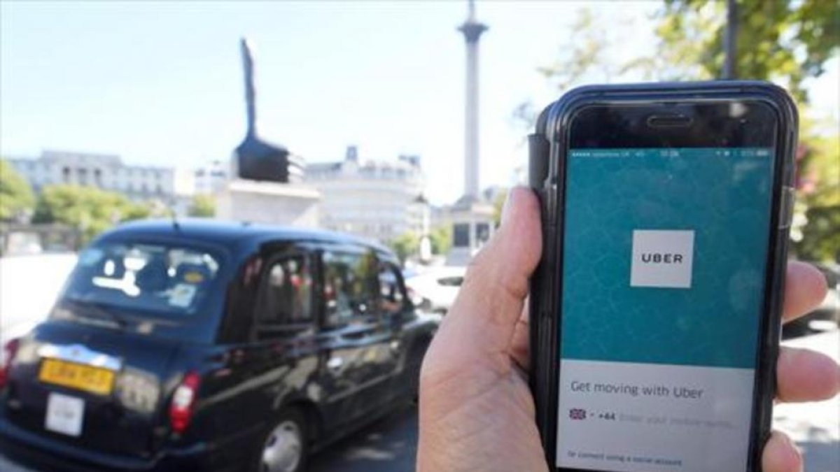 Un taxi de Londres pasa delante de un móvil con la aplicación de Uber activada, ayer.
