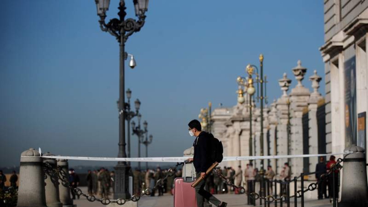 Un joven con su maleta y mascarilla pasa ante el Palacio Real de Madrid, vallado. JUAN CARLOS HIDALGO