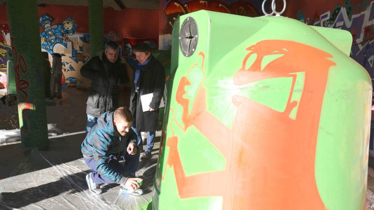El alcalde y el edil de Cultura observan al grafitero en uno de los contenedores de vidrio.