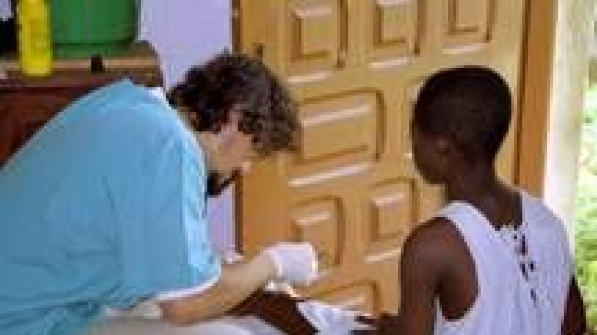 Un voluntario de una organización no gubernamental cura la pierna de una niña guineana herida
