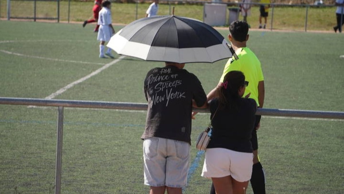 Dos aficionados disfrutan del fútbol este sábado en León protegidos del calor por una paragüas. J. NOTARIO