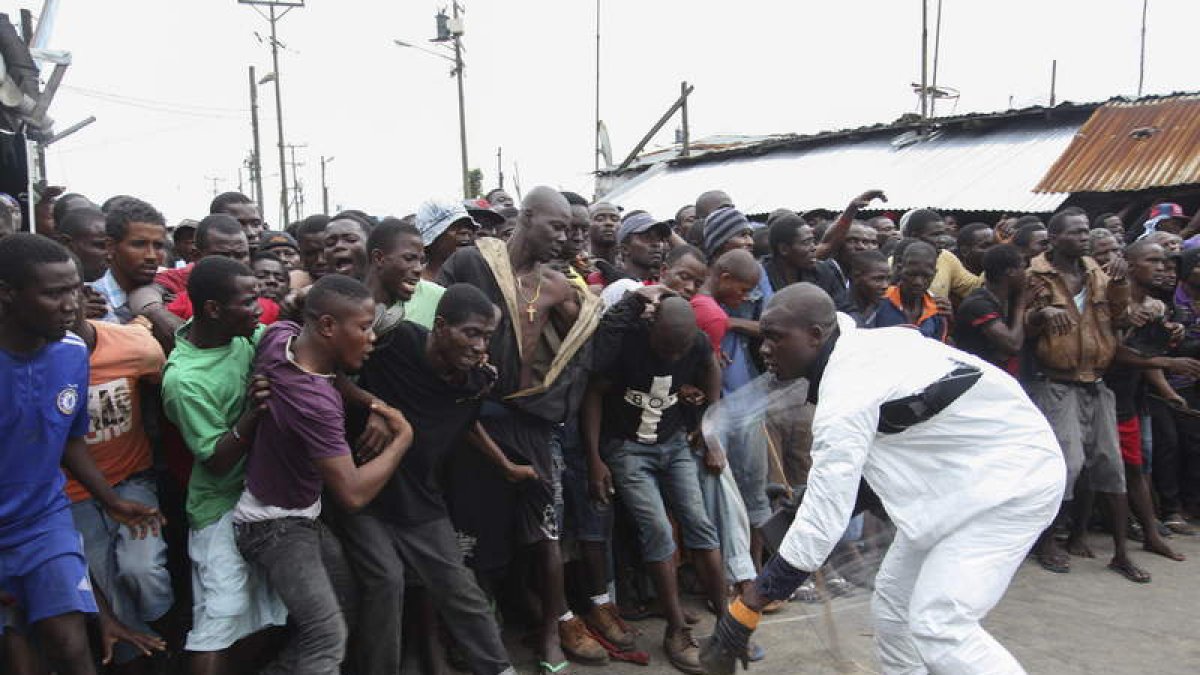 Un policía protegido controla a varias personas que esperan la entrega de alimentos en Liberia.