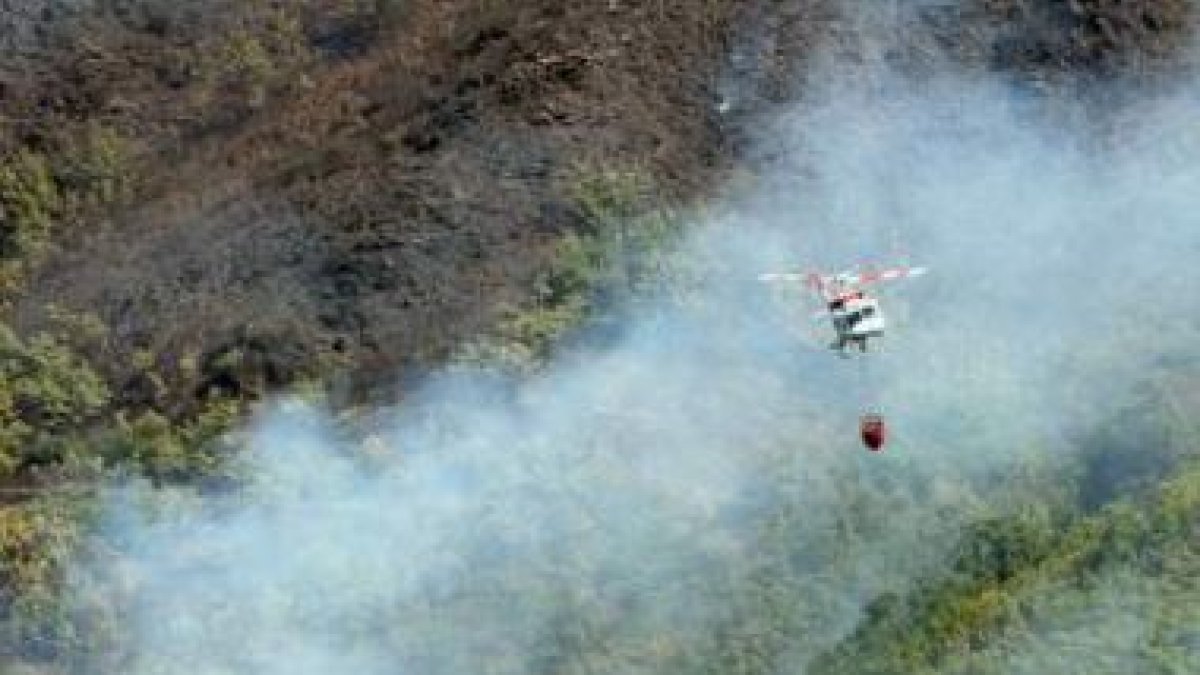 Un helicóptero, en medio del humo, sobrevuela el robledal en la zona de San Clemente.