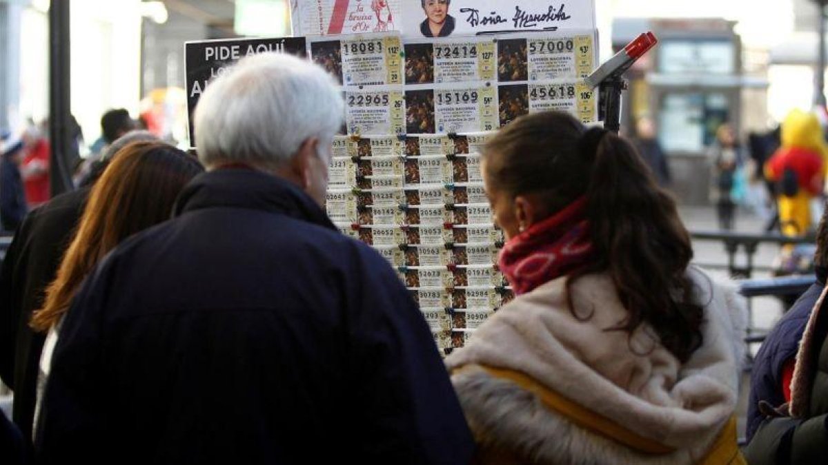 Varias personas adquieren décimos de Lotería de Navidad en los puestos instaldados en la Puerta del Sol (Madrid) este 21 de diciembre