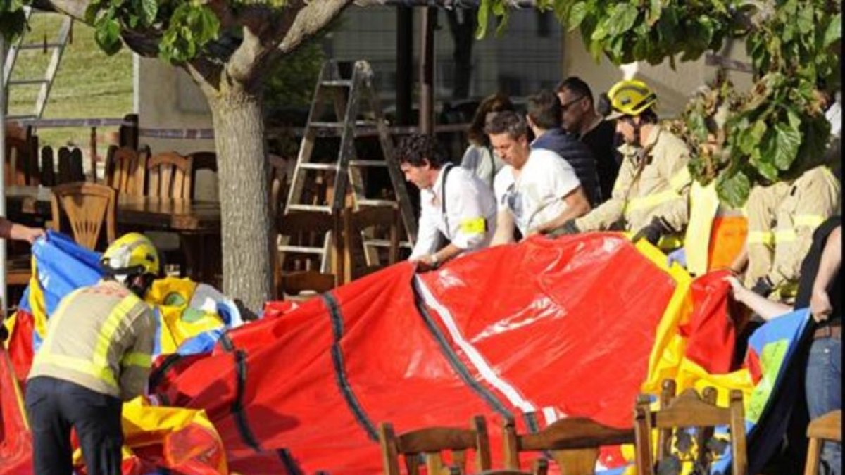 Varios operarios y bomberos retiran el castillo hinchable tras su trágico vuelo.