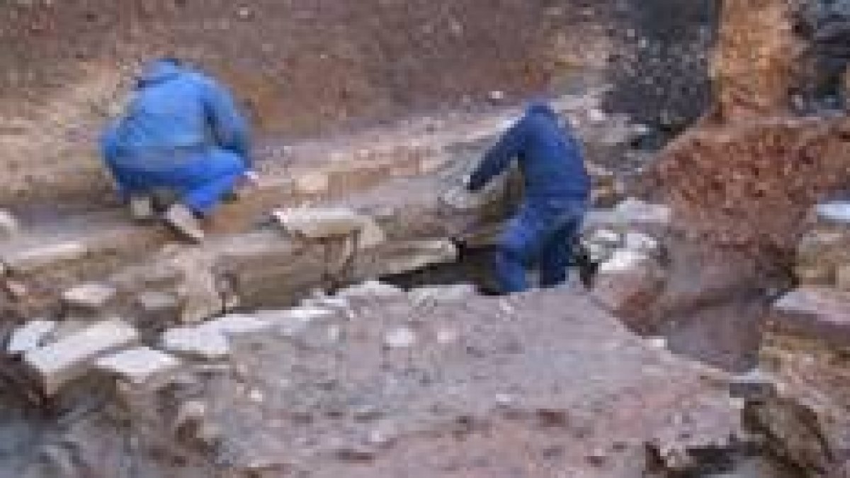 Dos operarios trabajan junto al pavimento de piedra tipo canto de río encontrado en el solar