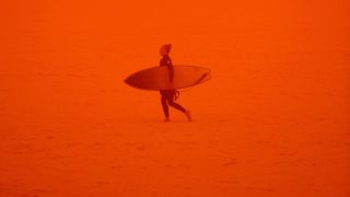 Una surfista recorre hoy la Playa Bondi durante una tormenta de polvo.