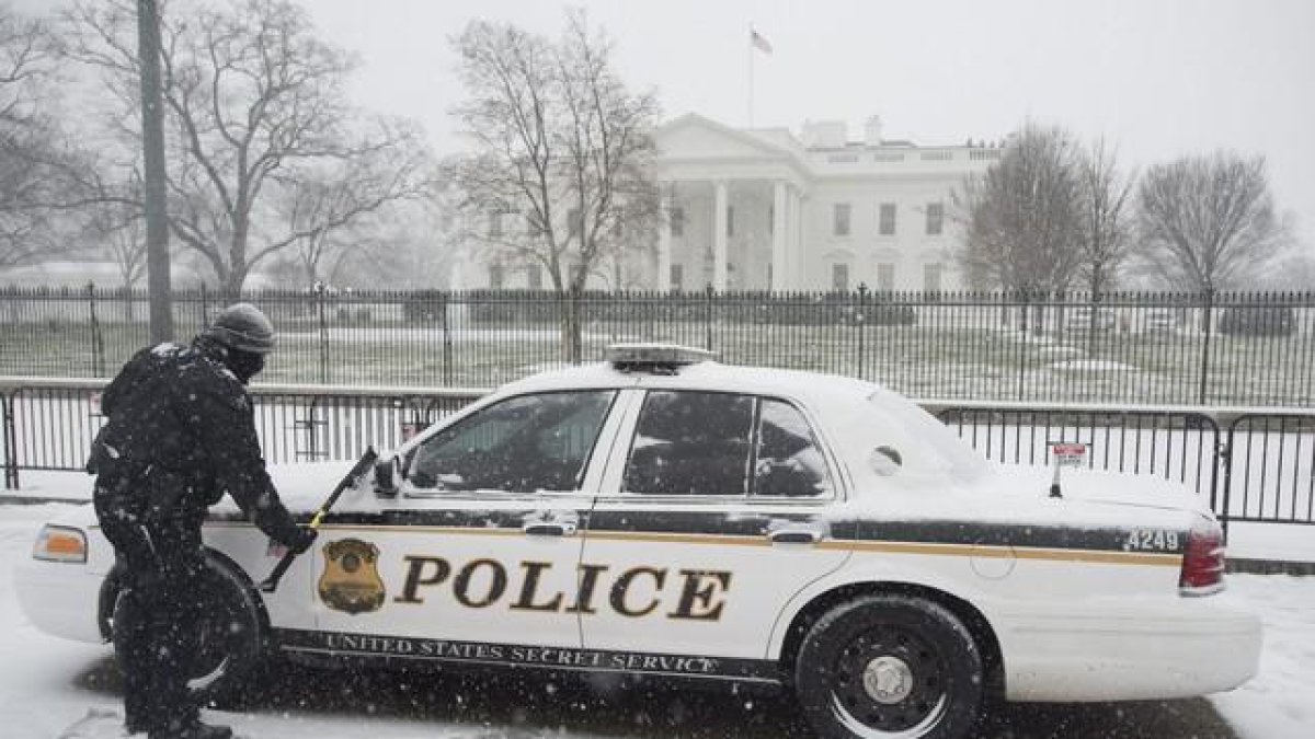 Un miembro del servicio secreto limpia la nieve de un vehículo en la Avenida Pennyslvania.