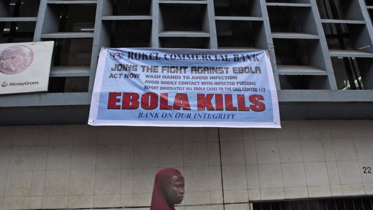 Una mujer, bajo un anuncio de alerta sobre el ébola.