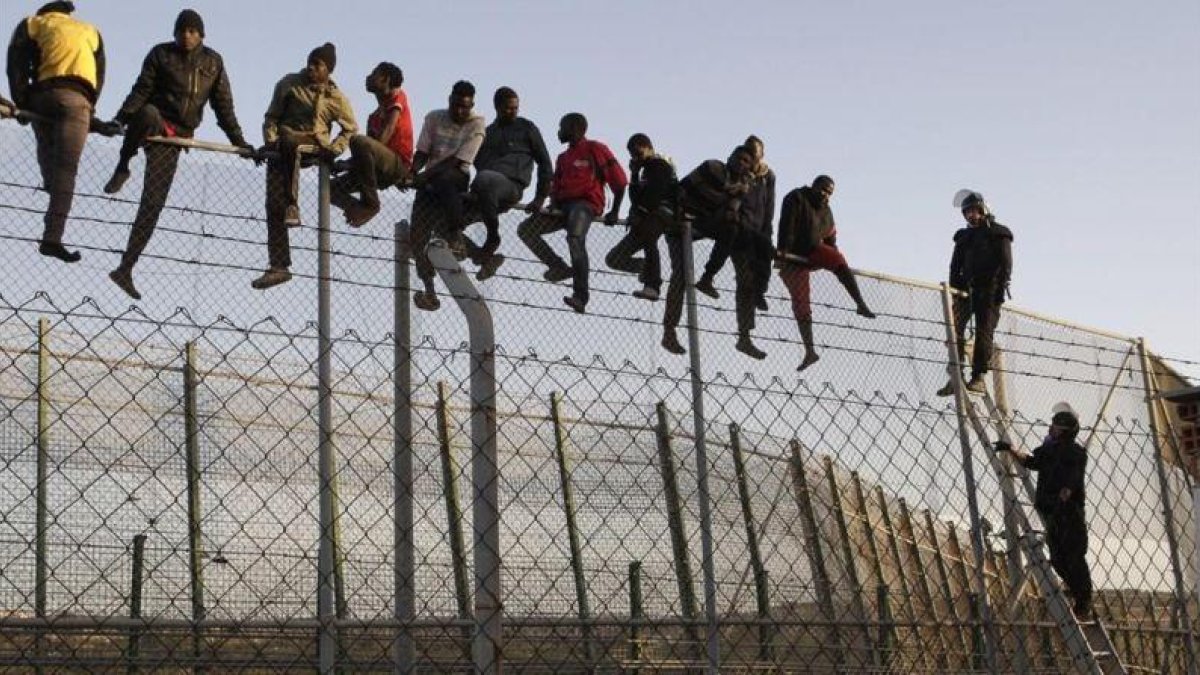Policías españoles tratan de disuadir a inmigrantes encaramados a la valla de Melilla, fronteriza con Marruecos.