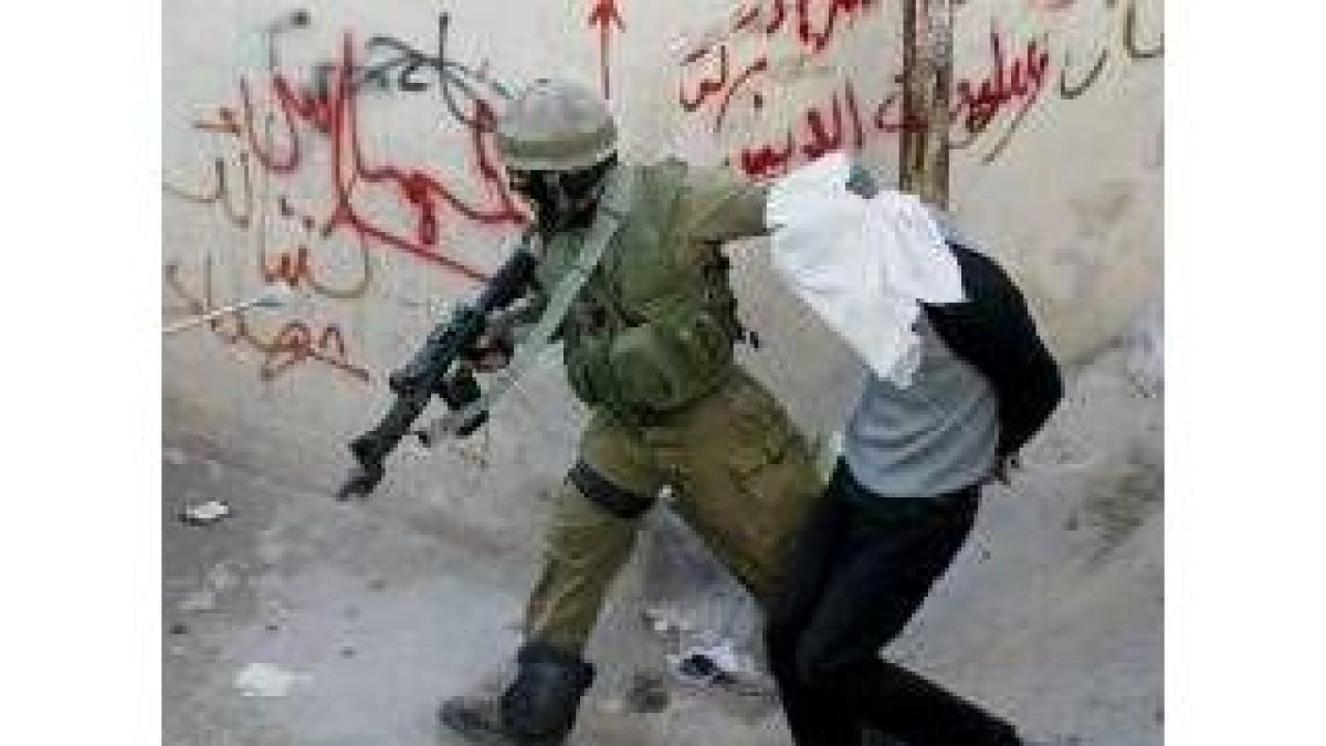 Un soldado conduce, esposado y encapuchado, a un palestino detenido