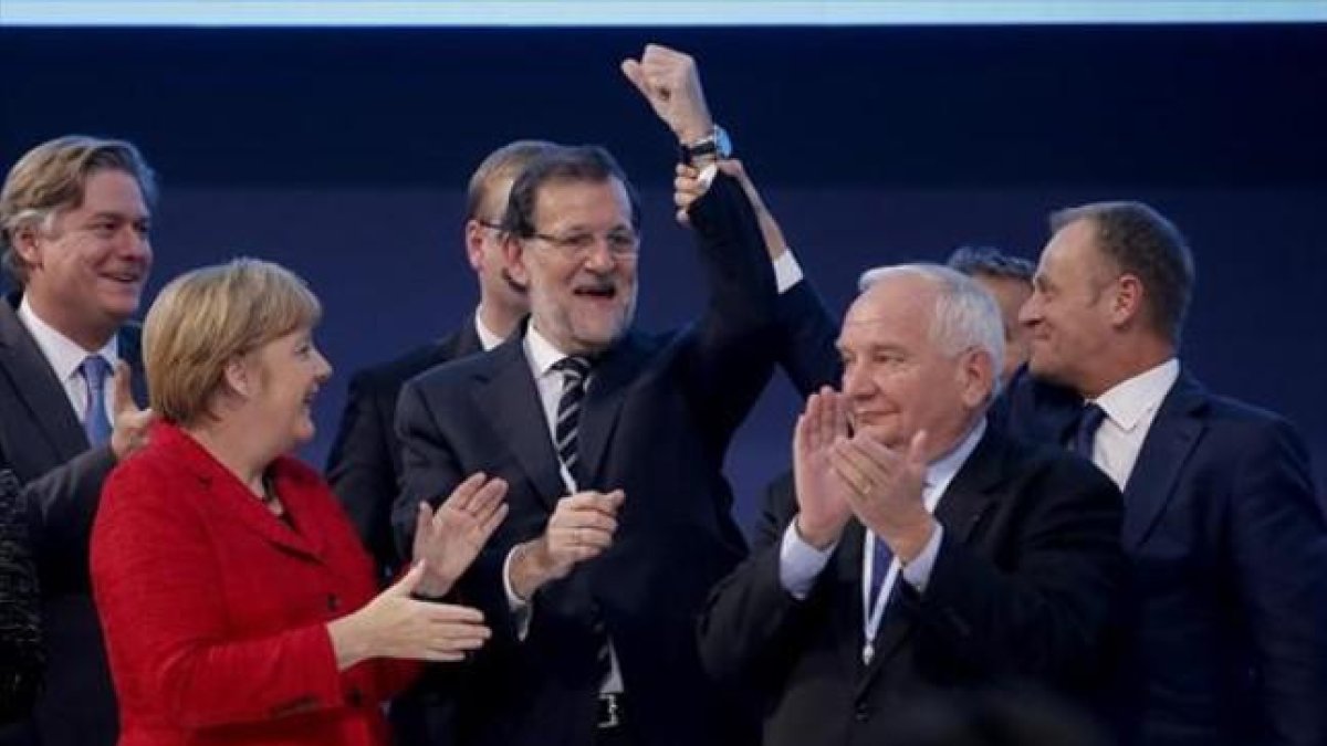 El presidente del Consejo Europeo, Donald Tusk, levanta el brazo de Rajoy en presencia de Angela Merkel y otros dirigentes populares europeos.