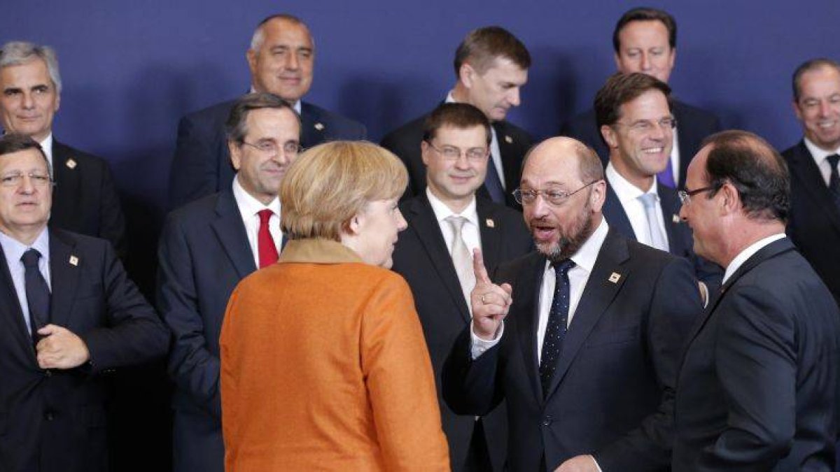 El presidente del Parlamento Europeo, Martin Schulz, se dirige a la cancillera alemana, Angela Merkel, ante el presidente francés, François Hollande (de espaldas), durante la foto de familia, el jueves en Bruselas.