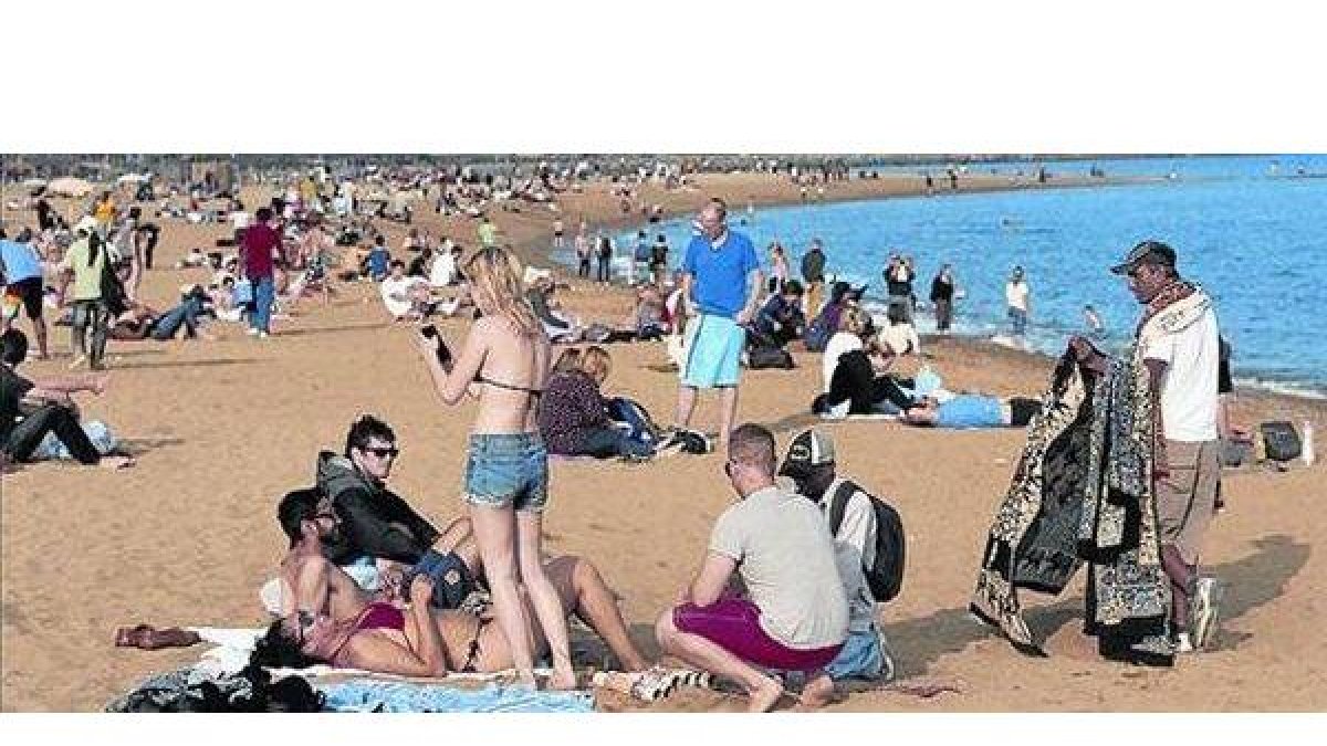 Turistas en la playa de la Barceloneta, aprovechando un día radiante.