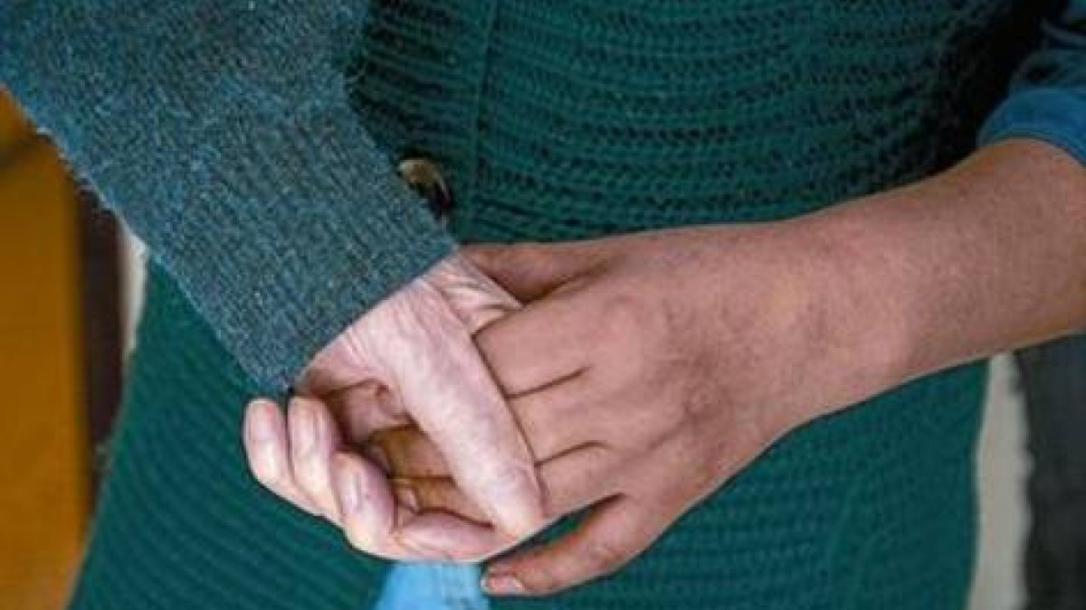 Un anciano con alzhéimer coge la mano de la persona que lo asiste.