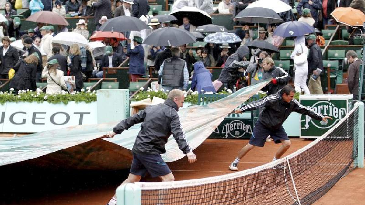 Operarios del torneo parisino extienden las lonas sobre la pista para preservarla de la lluvia durante la final Nadal-Djokovic.