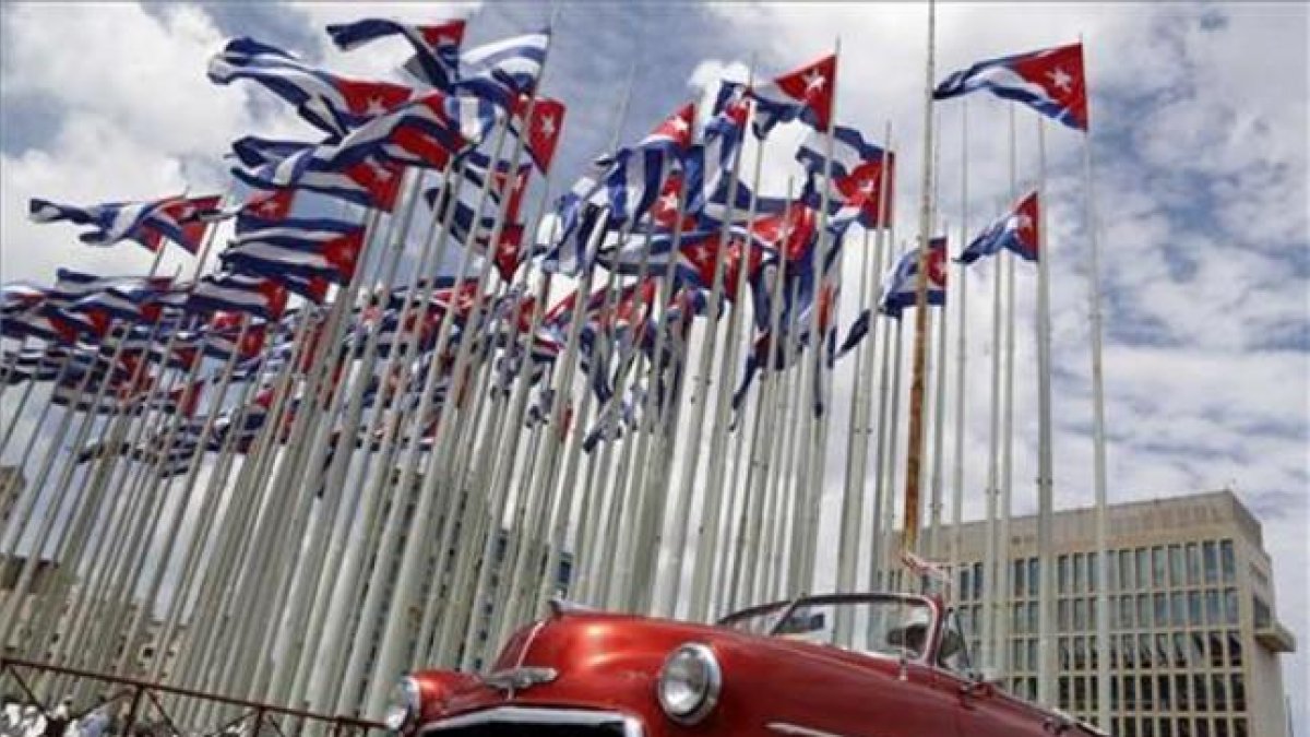 Un coche clásico americano pasa al lado de la embajada estadounidense en La Habana, donde ondean decenas de banderas de Cuba.
